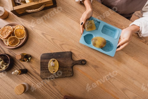 Preview: top view of cropped african american woman holding silicone mold with handmade soap near chopping