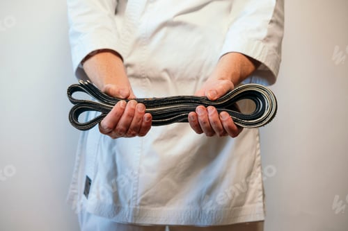 Preview: Martial artist presenting folded black belt forward.