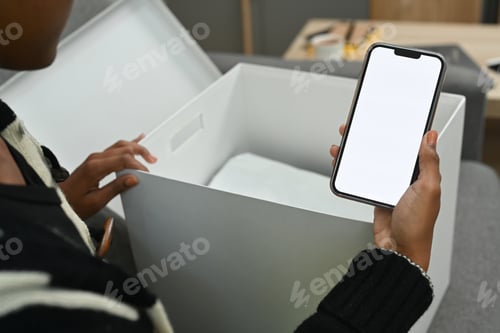 Preview: Close up view of female customer unpacking parcel f and using smart phone for giving feedback.