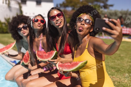 Preview: Diverse group of female friends taking selfie with watermelon sitting at the poolside
