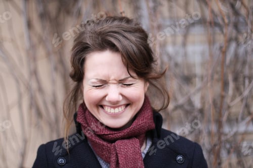 Preview: Portrait of a young smiling brunette girl in a coat and a burgundy scarf standing on the street.