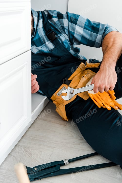 Preview: cropped view of repairman holding adjustable wrench near kitchen cabinet