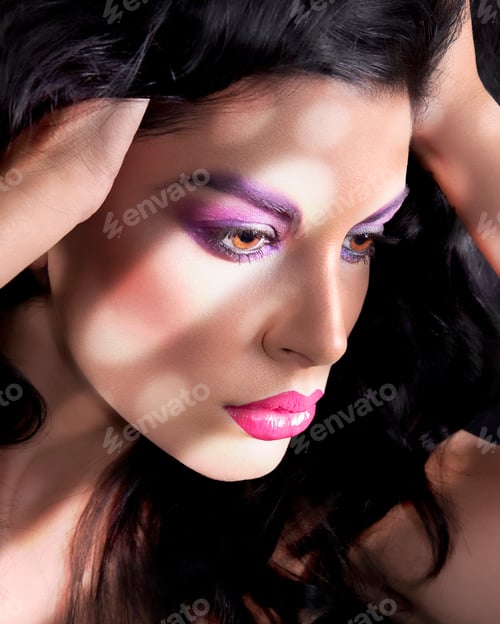 Preview: Close-up of a woman with dramatic purple eyeshadow and pink lipstick in a thoughtful pose.