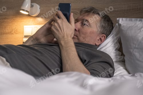 Preview: Middle-aged man businessman lies in bed and immediately after waking up reads the news on the phone.