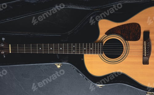 Preview: Acoustic guitar in a protective case on a dark background, top view.