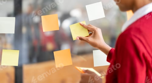 Preview: Closeup image of businesswoman hand sticking adhesive notes on glass wall.