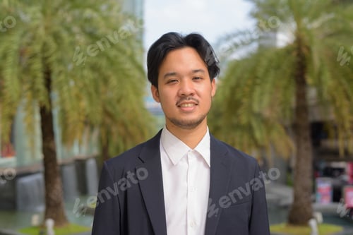 Preview: Portrait of happy Asian businessman smiling outdoors in the city