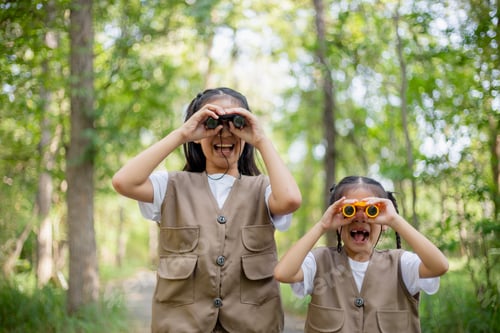 Preview: Happy Little Asian girls looking ahead and smiling child with the binoculars in the park.