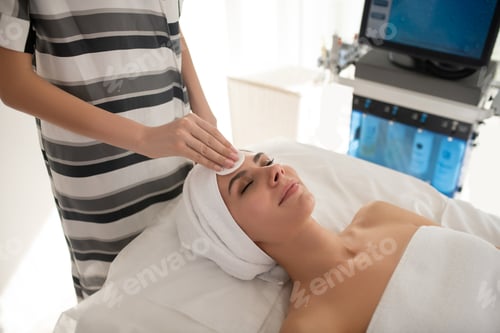 Preview: Cosmetologist in striped shirt cleaning clients face