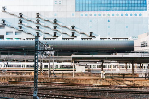 Preview: Modern railway station platform with commuter train and modern geometric building in the city