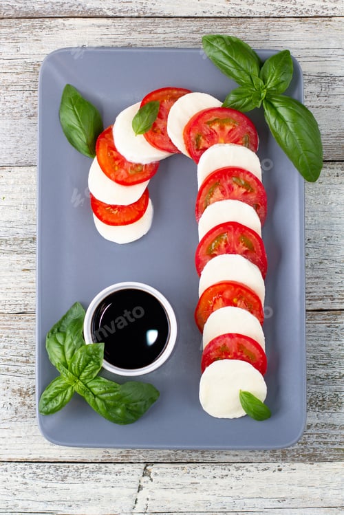 Preview: Christmas caprese salad in form of candy cane. Mozzarella and tomato on grey plate served