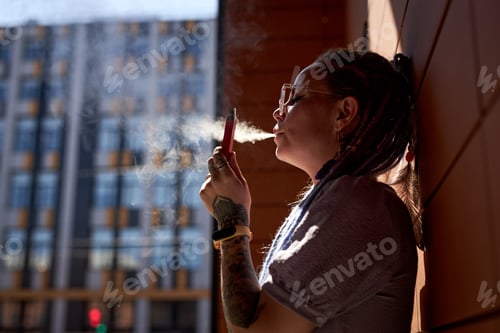Preview: Side view of young woman standing by wall of building and smoking