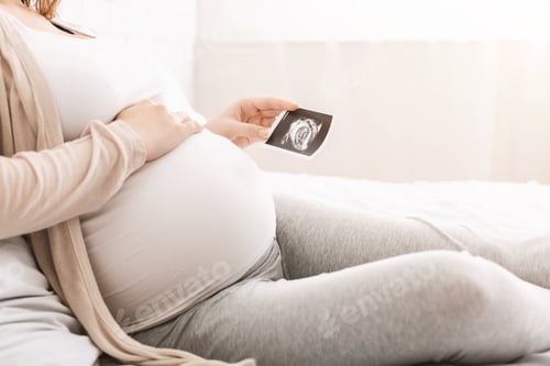 Preview: Pregnant woman touching belly and looking at sonography