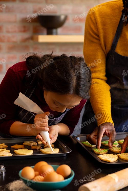 Preview: Focused diverse couple in aprons decorating christmas cookies in kitchen, copy space