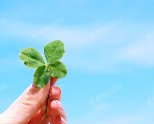 Preview: Woman is holding a four leaf clover against blue sky. Feeling lucky. Space for copy, text
