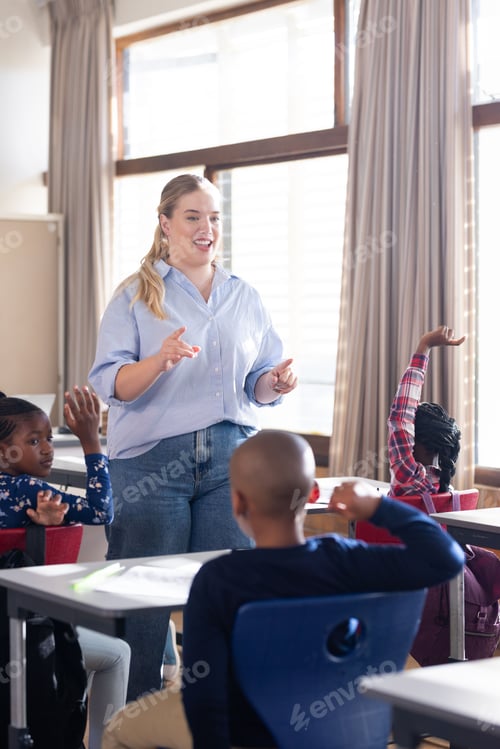 Preview: In school, female teacher engaging with diverse students raising hands in classroom discussion