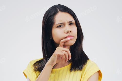 Vista previa: What does this mean. Studio shot of a young woman looking thoughtful against a gray background.