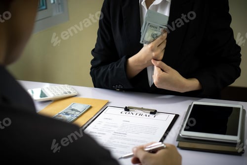 Preview: A business woman takes a dollar bill from a pocket in a suit to bribe an Land Department officer for