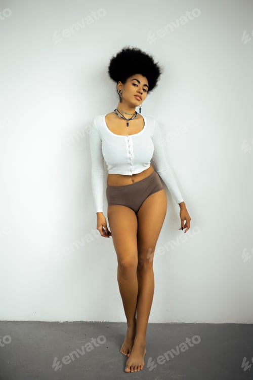 Preview: full length of barefoot african american woman in long sleeve shirt and panties standing near white