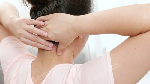 Preview: Back view of Asian woman using hands to massage the nape of her neck in physical therapy to reduce p