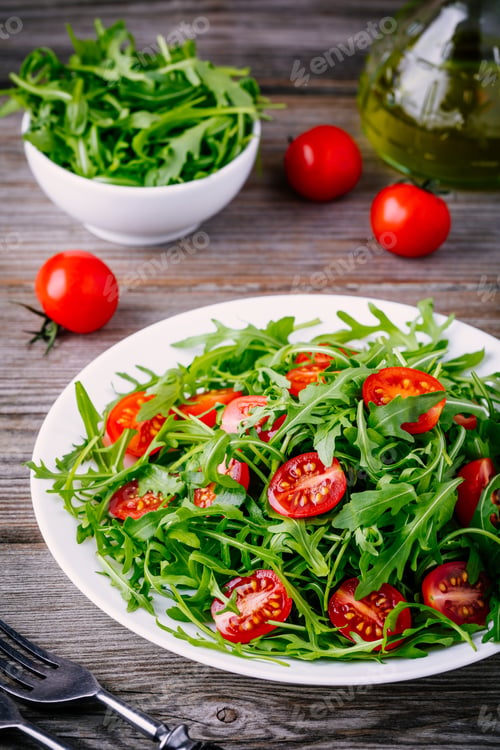 Preview: fresh green salad with arugula and red tomatoes on wooden background