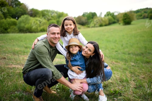 Visualização: Família feliz com duas filhas pequenas sentadas ao ar livre na natureza da primavera, olhando para a câmera