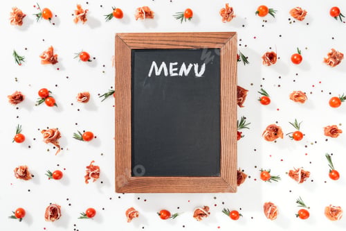 Preview: chalk board with menu lettering among tomatoes, prosciutto, spices and leaves