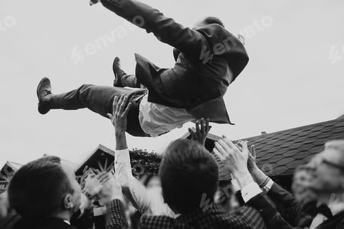Preview: Men tossing up groom at stylish wedding reception