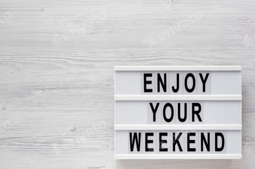 Preview: 'Enjoy your weekend' words on a modern board on a white wooden background, top view.