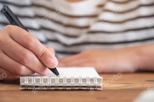 Preview: Closeup image of a woman's hand writing on blank notebook on wooden table