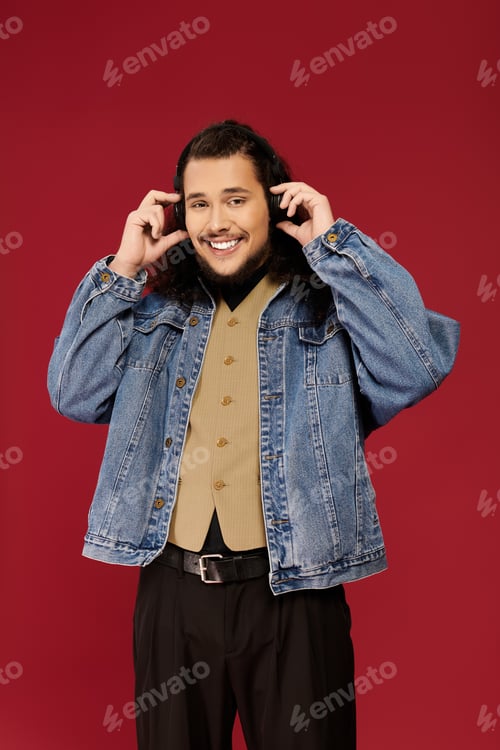 Preview: Charming young man with a beard enjoys music against a vibrant red backdrop