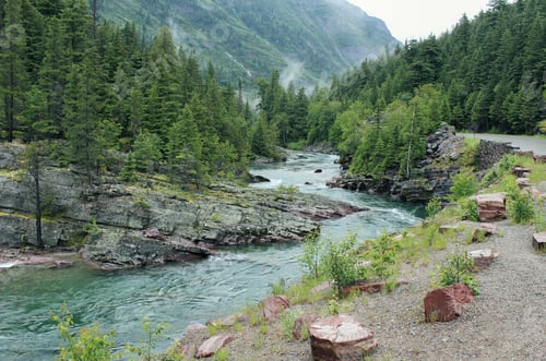 Preview: Curvy lake flowing down in the middle of rocky cliffs and hills with trees and a forested mountain