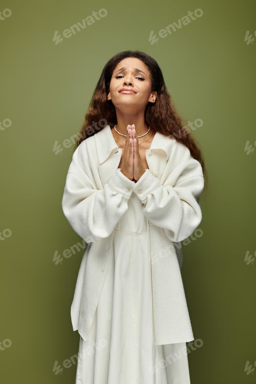 Preview: A woman in a white dress with a thoughtful expression standing against a green background