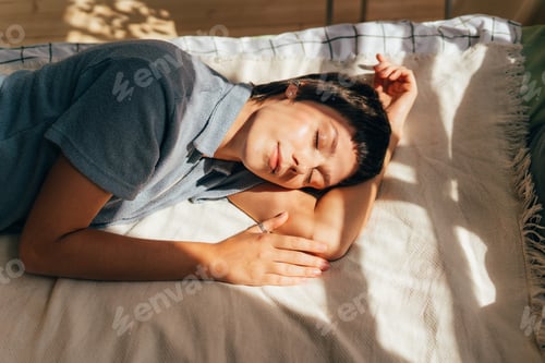 Preview: A woman lies relaxed on a bed in the light of summer sunbeams.