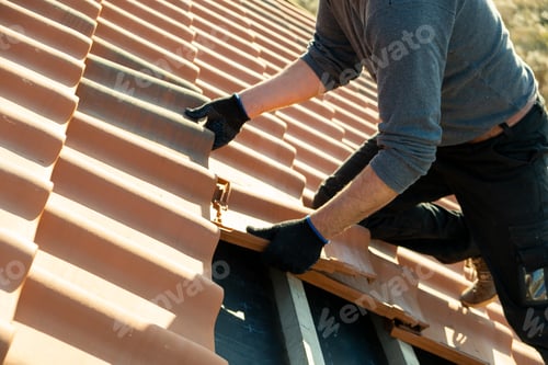 Preview: Closeup of worker hands installing yellow ceramic roofing tiles mounted on wooden boards
