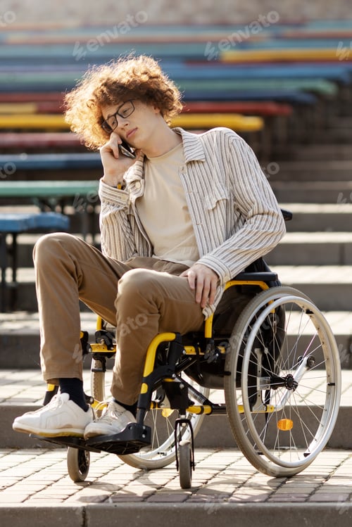 Preview: Sad, young disabled guy in a wheelchair talking on the phone. He is sitting in a chair