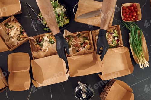 Preview: Burgers and vegetables. Man is packing food into the paper eco boxes. Indoors, restaurant