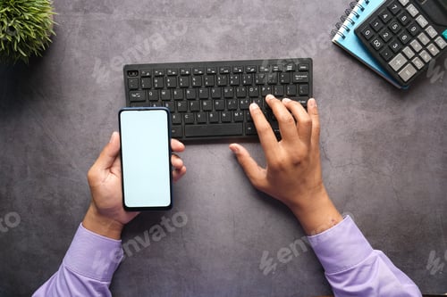 Preview: Top view of man hand holding smart phone with empty screen on office desk