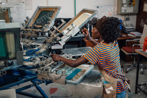 Preview: Interracial female worker manipulating silkscreen printing press at shop