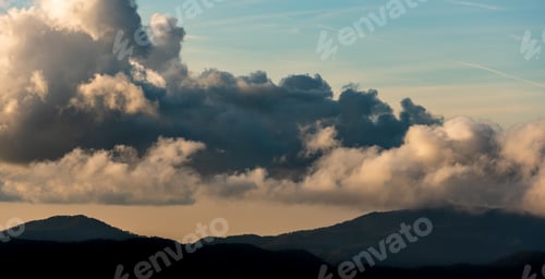 Preview: Silhouette of mountain peaks with fog and dramatic clouds. Colorful sunset.