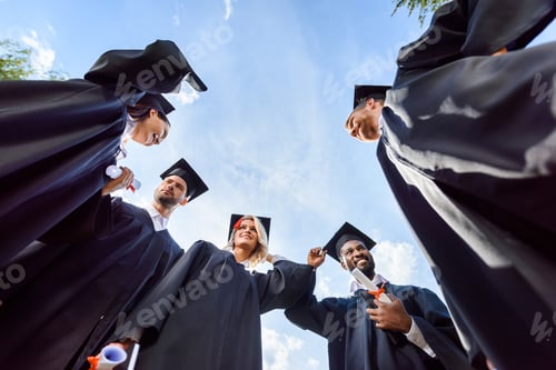 Preview: bottom view of happy young graduated students in front of blue sky