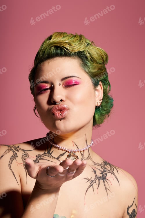 Preview: Vibrant young woman with colorful hair and stylish makeup blowing a kiss against a pink backdrop