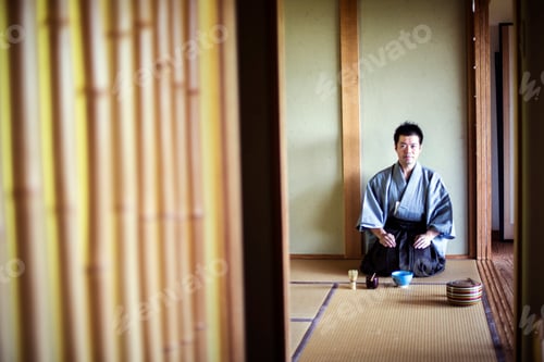 Preview: Japanese man wearing traditional kimono kneeling on tatami mat during tea ceremony.