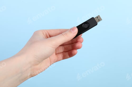 Preview: Woman holding USB flash drive on light blue background, closeup