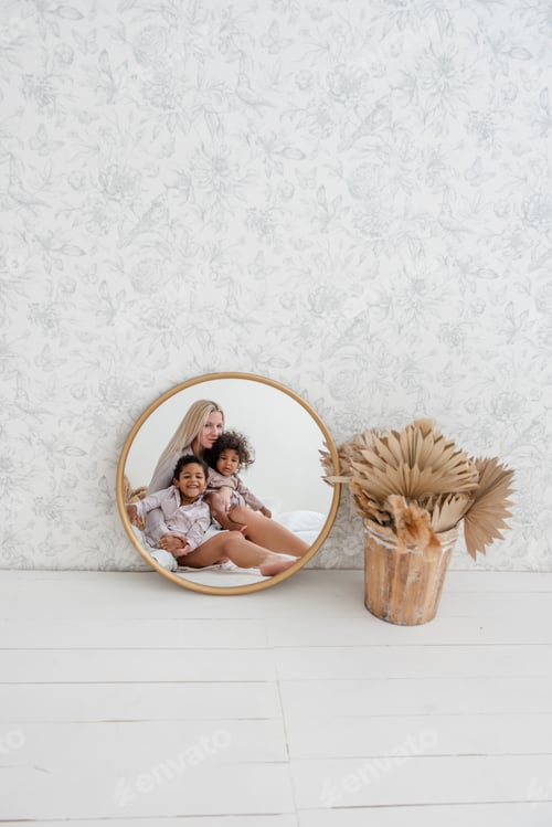 Preview: In round mirror Caucasian mother sitting on wooden floor with African American children