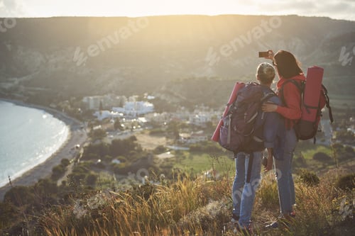 Preview: Female Campers With Bags Standing On Hill, Hugging And Making Selfie. Seashore On Background. Copy