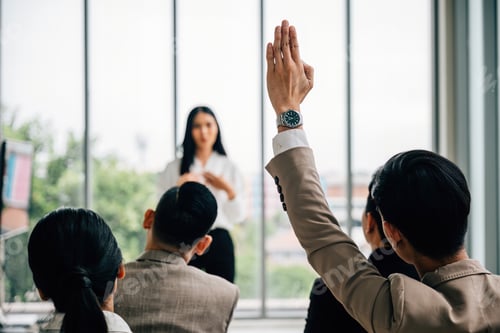 Preview: In a seminar classroom at a conference, a large group raises hands in participation. The engaged