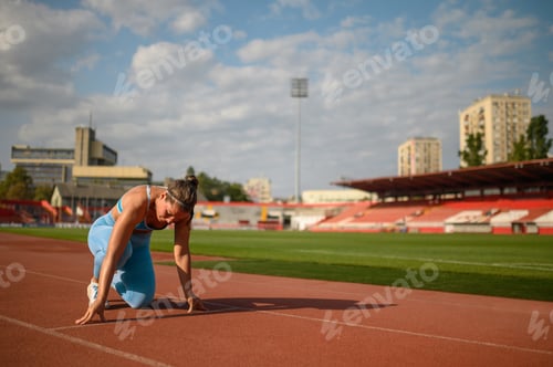Preview: Woman racer getting ready to start a race on a tartan race track at the stadium