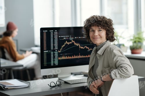 Preview: Young smiling female analyst sitting by workplace with computer monitor