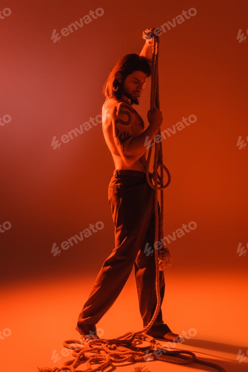 Preview: Full length of sexy tattooed model posing with rope on red background